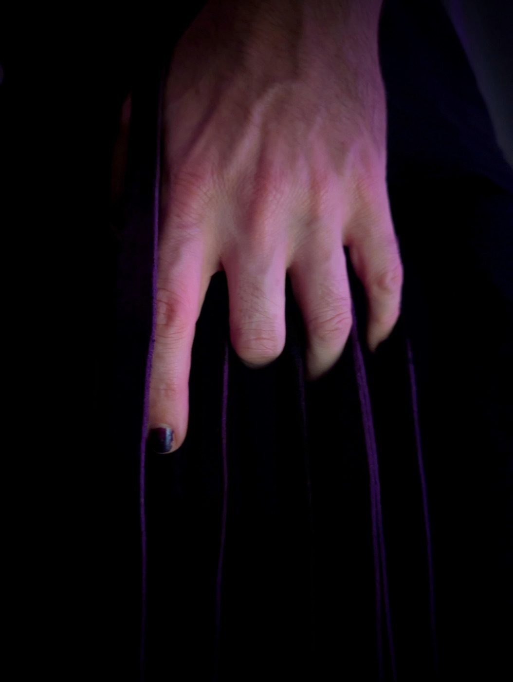A single hand resting across draped flogger falls, one fingertip catching the light.